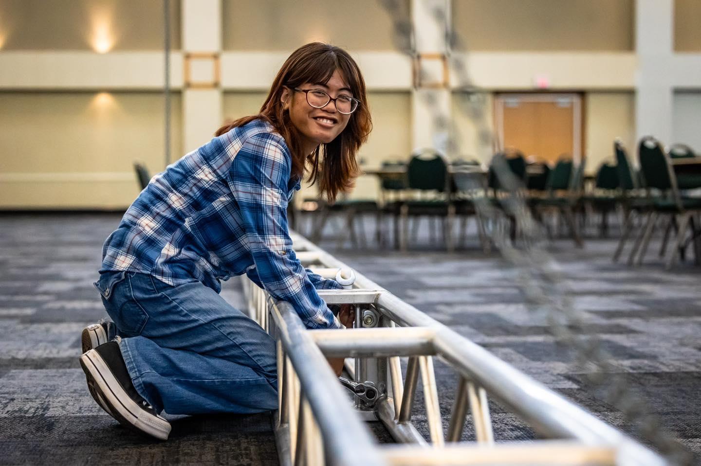 student smiles at camera while building a metal frame